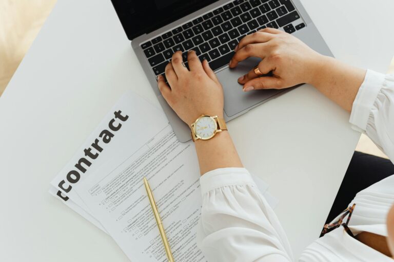 A woman using a laptop alongside a contract document on a desk, emphasizing business and legal themes.